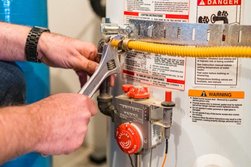 Plumber flushing a tank water heater during routine water heater maintenance in a Houston garage