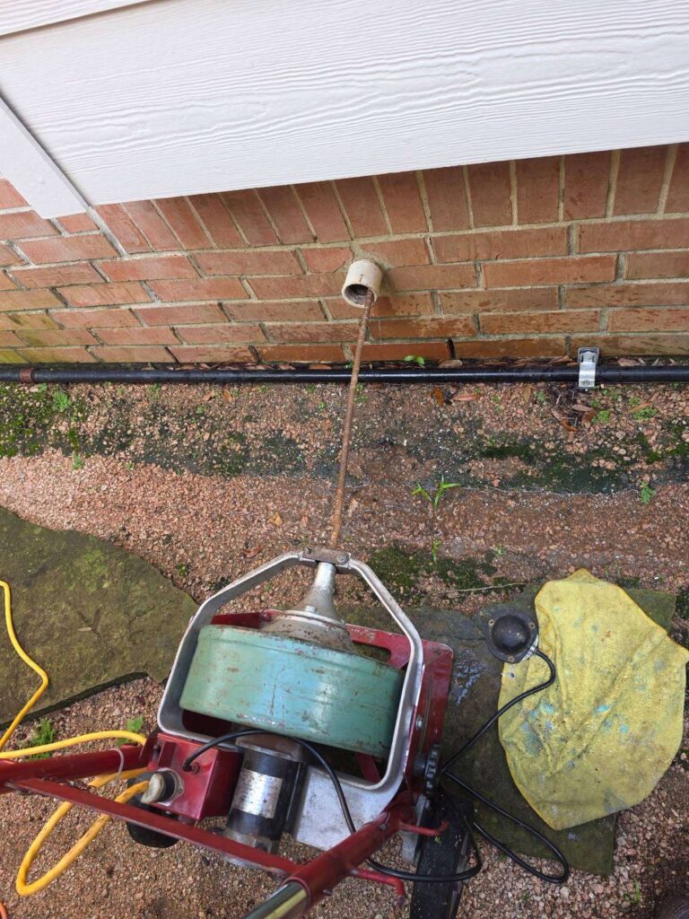Drain machine cable clearing a sewer line through the exterior cleanout at a River Oaks Houston home